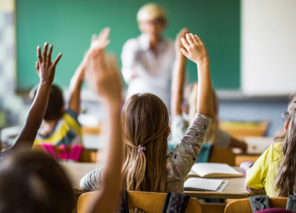 Rear view of elementary students raising their hands on a class.