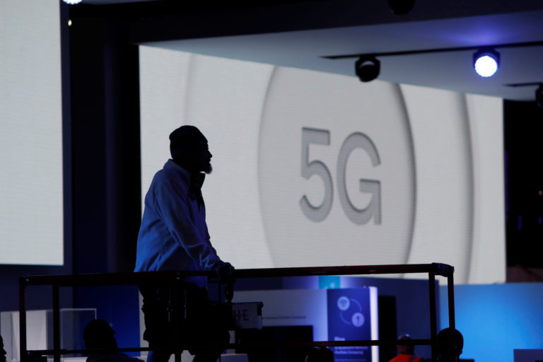 A worker is silhouetted in the Qualcomm booth as a video for 5G technology plays behind him at the Las Vegas Convention Ce...