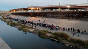 Migrants queue near the border wall after crossing the Rio Bravo river, as seen from Ciudad Juarez