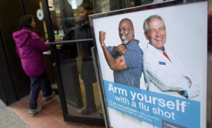 FILE PHOTO: People enter a pharmacy next to a sign promoting flu shots in New York