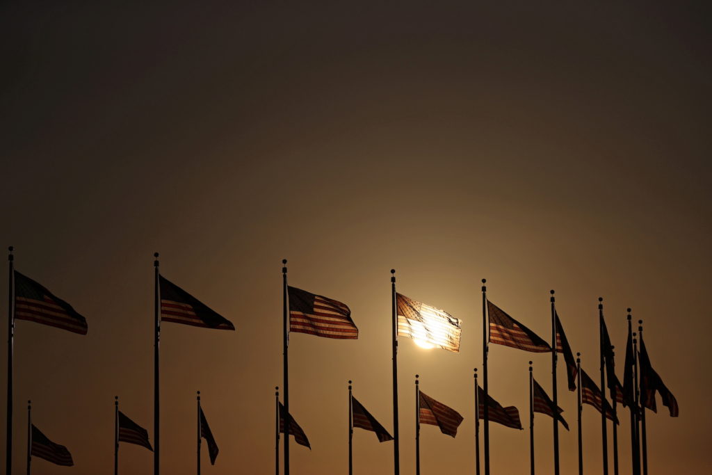 The sun sets behind the U.S. flags surrounding the Washington Monument