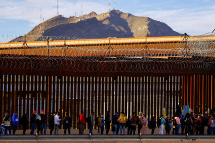 Migrants queue near the border fence, after crossing the Rio Bravo river, to request asylum in El Paso