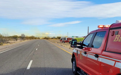 Emergency vehicles are seen as an overturned truck spews orange smoke in the background at I-10 Highway in Tucson