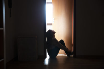 Backlit teenager sitting in a dark indoor doorway in contemplation