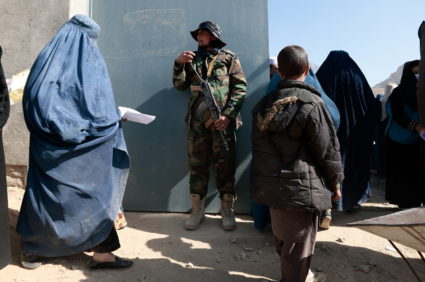 Taliban fighter stands on guard as displaced Afghan women walk into an UNHCR distribution center to receive aid supply on ...