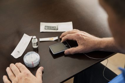 Over the shoulder shot of older man looking at his type-1 diabetes supplies on kitchen table.