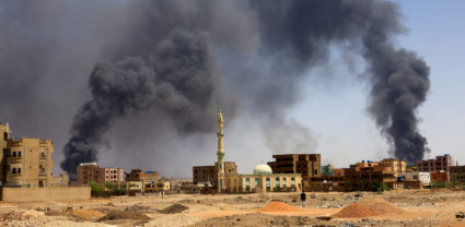 Man walks while smoke rises above buildings after aerial bombardment in Khartoum North