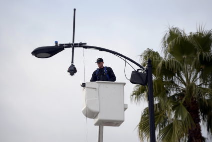 A worker puts up a surveillance camera on a street light pole along the route of the parade on Colorado Boulevard in prepa...