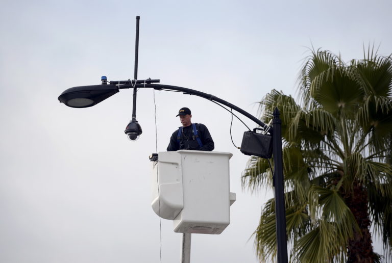 A worker puts up a surveillance camera on a street light pole along the route of the parade on Colorado Boulevard in prepa...