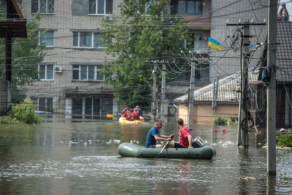 Local residents sail on boats at a flooded street during an evacuation from a flooded area after the Nova Kakhovka dam bre...