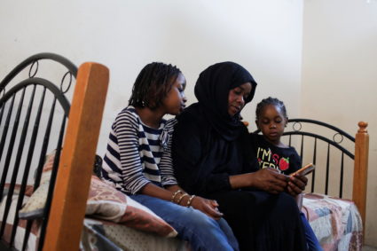 Sanaa Mahmoud, a Sudanese displaced woman who fled after the last crisis in Sudan's capital Khartoum, looks at her mobile phone next to her daughters Talia and Talien, after an interview with Reuters during their stay at a shelter in the district of Boulaq Al-Dakrour in Giza, Egypt May 13, 2023. Photo by Hadeer Mahmoud/REUTERS