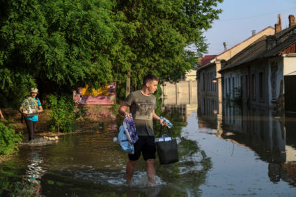 Local residents carry their belongings from a flooded house after the Nova Kakhovka dam breached, in Kherson