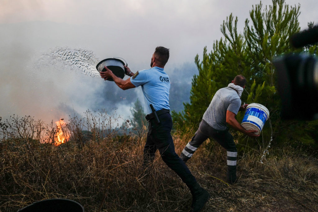 A police officer and a local resident throw buckets of water during a wildfire in Cascais