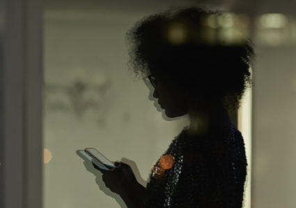 Reflection of young businesswoman checking smartphone in the office at night