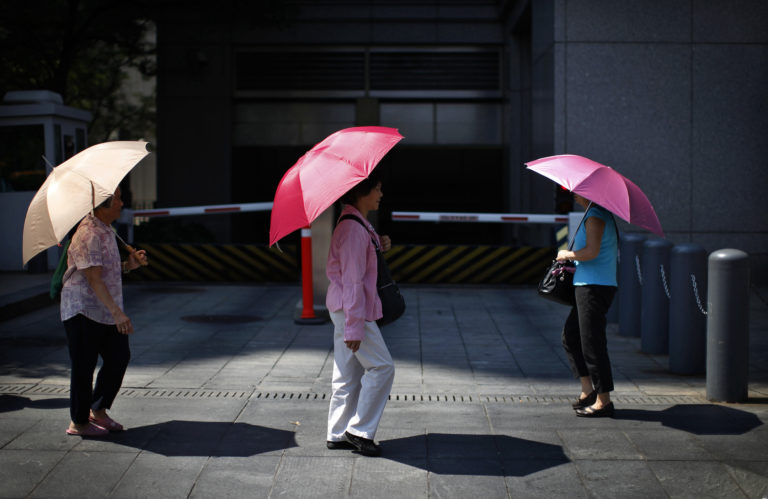 Women shield themselves from the midday sun in the Chinatown section of lower Manhattan in New York City