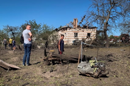 Local residents look at a part of a missile as they stand near residential buildings destroyed during a Russian military s...