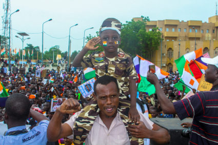 A man carries a child dressed in military uniform as he gathers with thousands of anti-sanctions protestors holding Nigerien flags and Russian flags in the capital Niamey, Niger August 20, 2023. The sign reads "all the people of Niger support 100% the CNSP". Photo by Mahamadou Hamidou/REUTERS