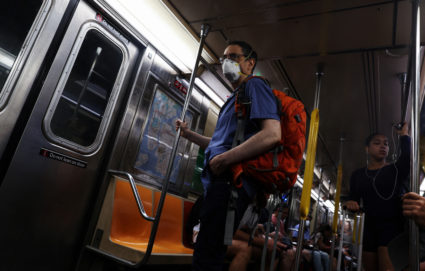 A man wearing a protective face mask holds on to a pole while riding a subway in New York City,