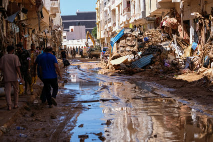 People walk in the mud between the rubbles, after a powerful storm and heavy rainfall hit Libya, in Derna