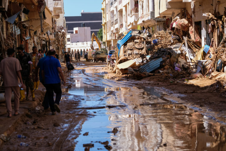 People walk in the mud between the rubbles, after a powerful storm and heavy rainfall hit Libya, in Derna