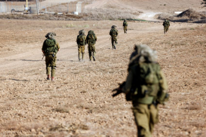 Israeli soldiers walk on grassy terrain near Israel's border with Gaza in southern Israel