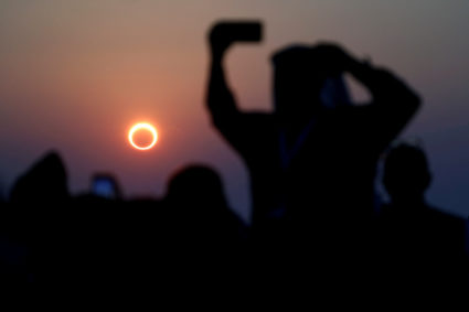 FILE PHOTO: People take photos with their smartphones as they monitor the annular solar eclipse on Jabal Arba (Four Mounta...