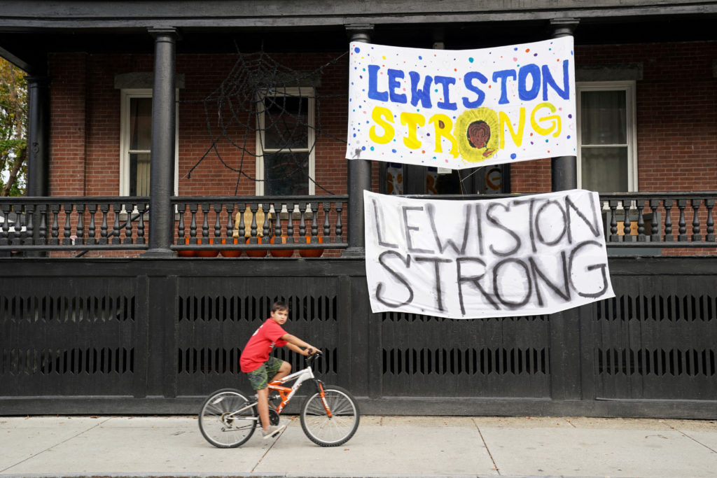 A boy cycles past "Lewiston strong" banners, as the search for the suspect in the deadly mass shootings continues, in Lewi...