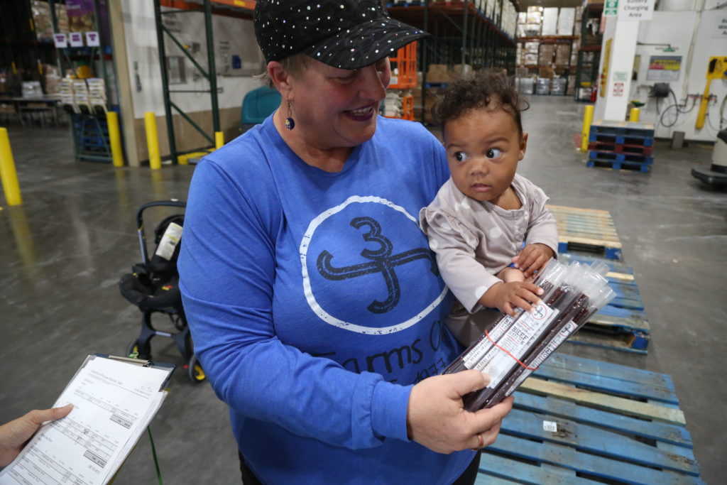 Jennifer Hernandez, 46, holds her granddaughter Jada as they deliver a package of beef sticks that will go to an Oklahoma school as part of the local food for local schools program. Photo by Adam Kemp, PBS NewsHour