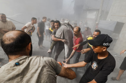 A Palestinian man carries a casualty at the site of Israeli strikes on houses, in Khan Younis