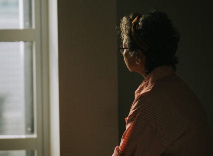 lonely asian chinese senior woman standing in the dark behind the window looking