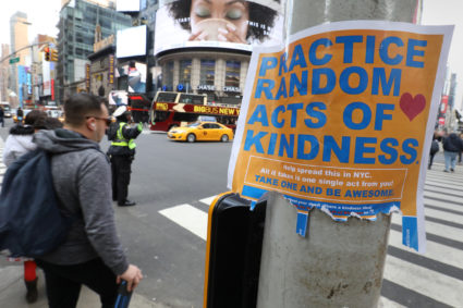 People walk past a "Practice Random Acts of Kindness" sign in Times Square Manhattan, New York