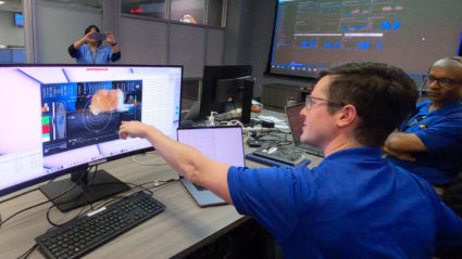 Members of NASA's Deep Space Optical Communications (DSOC) team react to the first high-definition streaming video to be sent via laser from deep space at the agency's Jet Propulsion Laboratory. One person points to an image on a monitor that shows Taters, an orange cat that stars in the brief video while chasing a laser pointer.