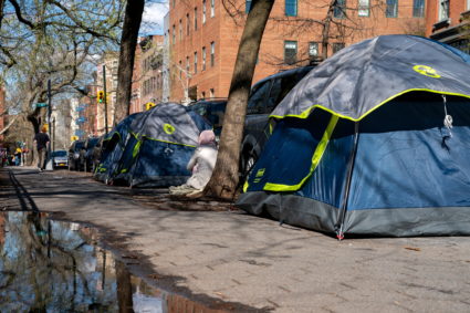 A person seats between tents belonging to homeless people who were removed from an encampment on East 9th Street earlier this week and have relocated a block adjacent to Tompkins Square Park in Manhattan in New York City, U.S., April 8, 2022. Photo by David 'Dee' Delgado/REUTERS