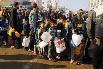 Palestinian children queue as they wait to collect drinking water, amid shortages of drinking water, as the conflict betwe...