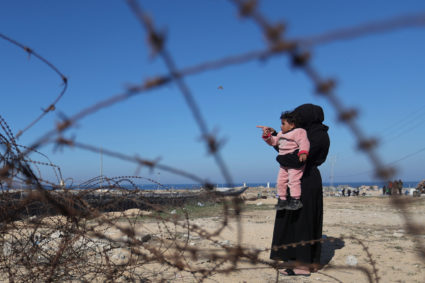 A displaced Palestinian woman, who fled her house due to Israeli strikes, holds a child near the border with Egypt, in Raf...