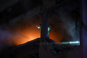 A person gestures as he stands on the damaged building at the site of an explosion, in the Beirut suburb of Dahiyeh