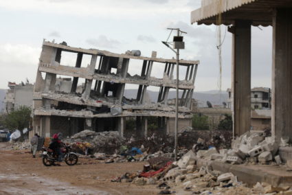 People ride a motorbike past damaged buildings in Jandaris