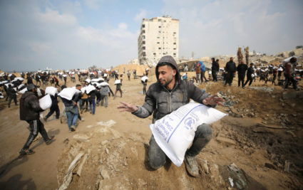 Palestinians carry bags of flour they grabbed from an aid truck near an Israeli checkpoint in Gaza City
