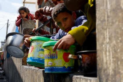 Palestinian children wait to receive food cooked by a charity kitchen, in Rafah