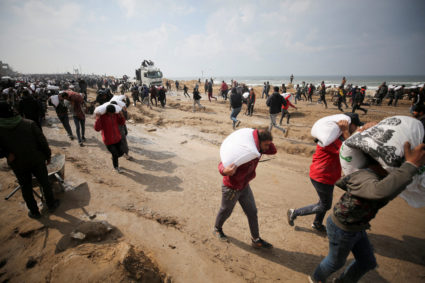 FILE PHOTO: Palestinians carry bags of flour they grabbed from an aid truck near an Israeli checkpoint in Gaza City