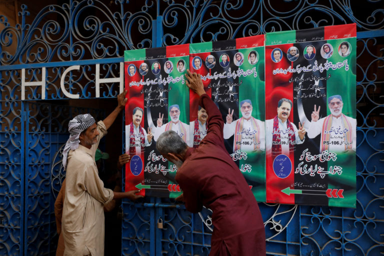 Workers hang campaign posters of a political party, ahead of general elections, in Karachi