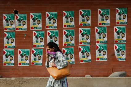 Woman walks past a wall with the campaign posters of political party, ahead of general elections, in Karachi