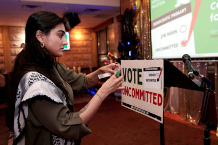 Activist Natalia Latif tapes a Vote Uncommitted sign on the speaker's podium during an uncommitted vote election night gat...