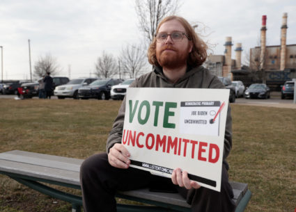 Listen To Michigan volunteer Eric Peter-Bull sits outside a polling station holding a sign that encourages people to vote ...