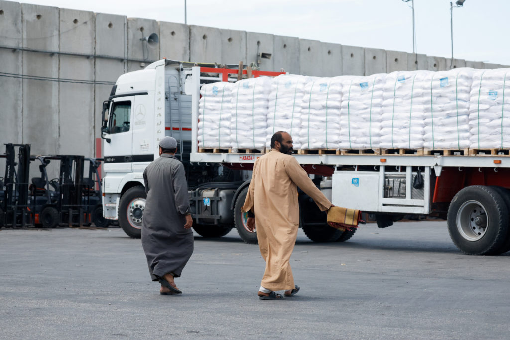 Drivers walk next to a truck carrying humanitarian aid bound for the Gaza Strip, as it waits at the Kerem Shalom crossing