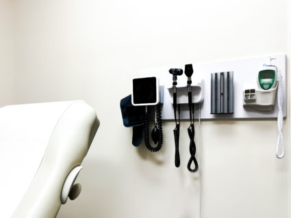 access to medical care: wall-mounted panel of medical diagnostic equipment beside standard patient examination chair