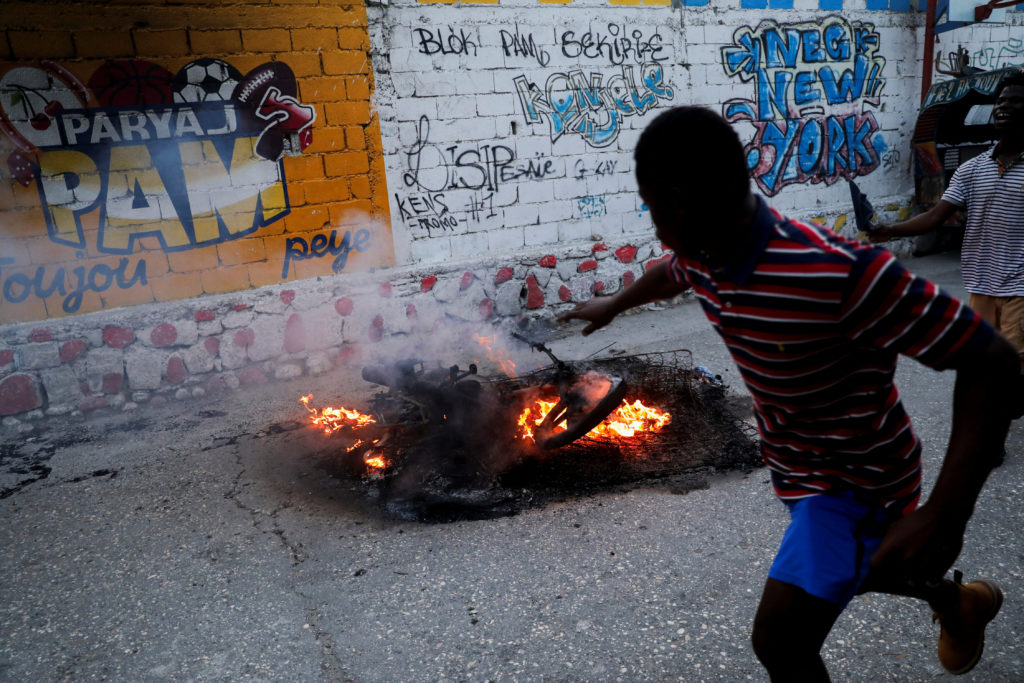 FILE PHOTO: Men run next to a pile of burning mattresses and the remains of the motorcycle of suspected gang leader Makand...