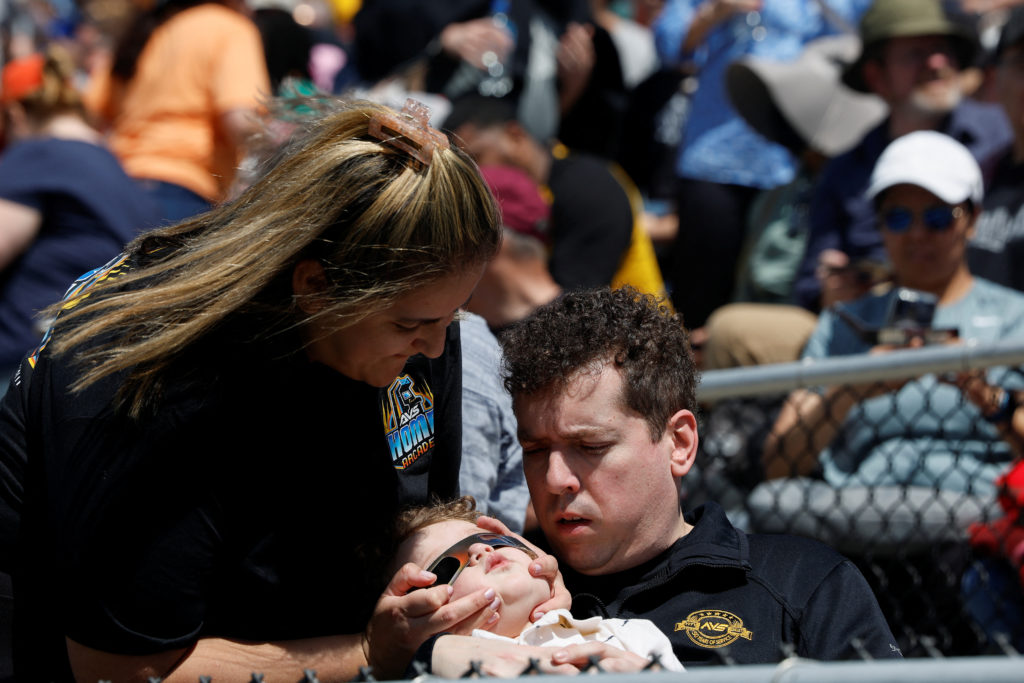 A woman holds a pair of eclipse glasses on a child's face at Saluki Stadium, as the moon partially blocks the sun, ahead of a total solar eclipse, where the moon will blot out the sun, in Carbondale, Illinois, U.S. April 8, 2024. Photo by Evelyn Hockstein/Reuters