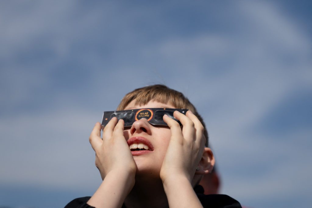 People watch the partial solar eclipse, where the moon partially blots out the sun, at Liberty Island in New York City