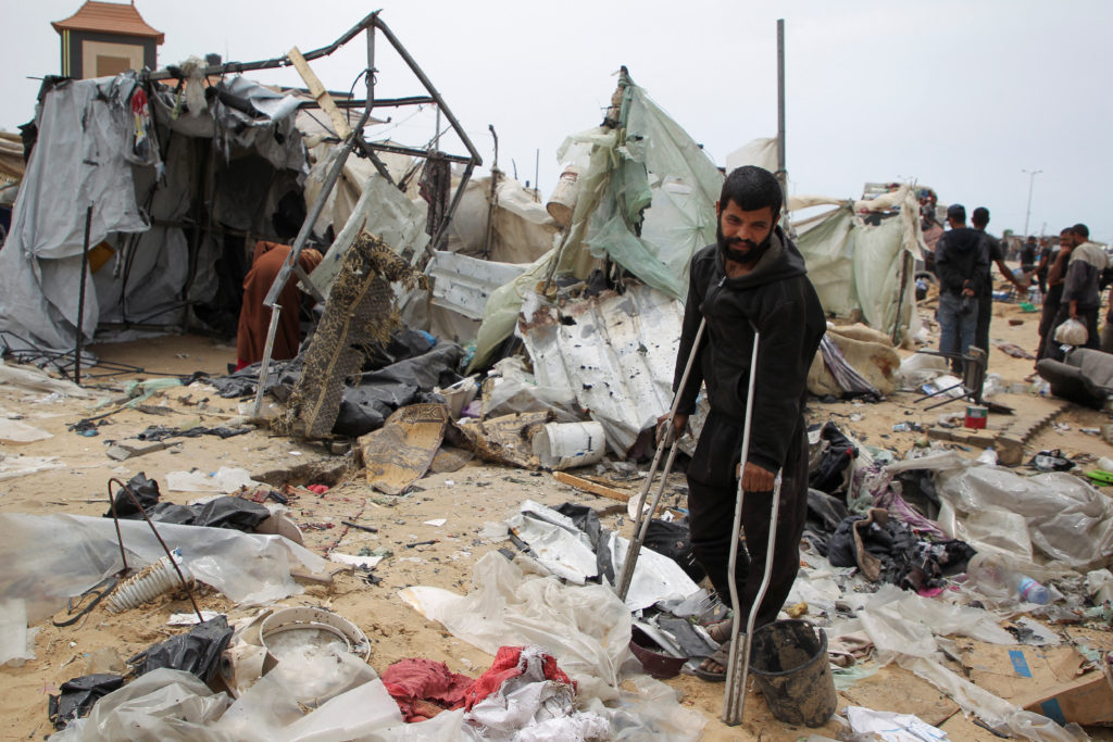 A man looks on as Palestinians inspect a tent camp damaged in an Israeli strike during an Israeli military operation, in R...